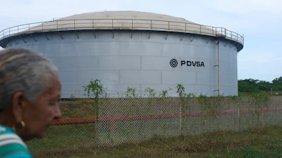 Large cylindrical PDVSA storage tank behind chain-link fence with woman in foreground