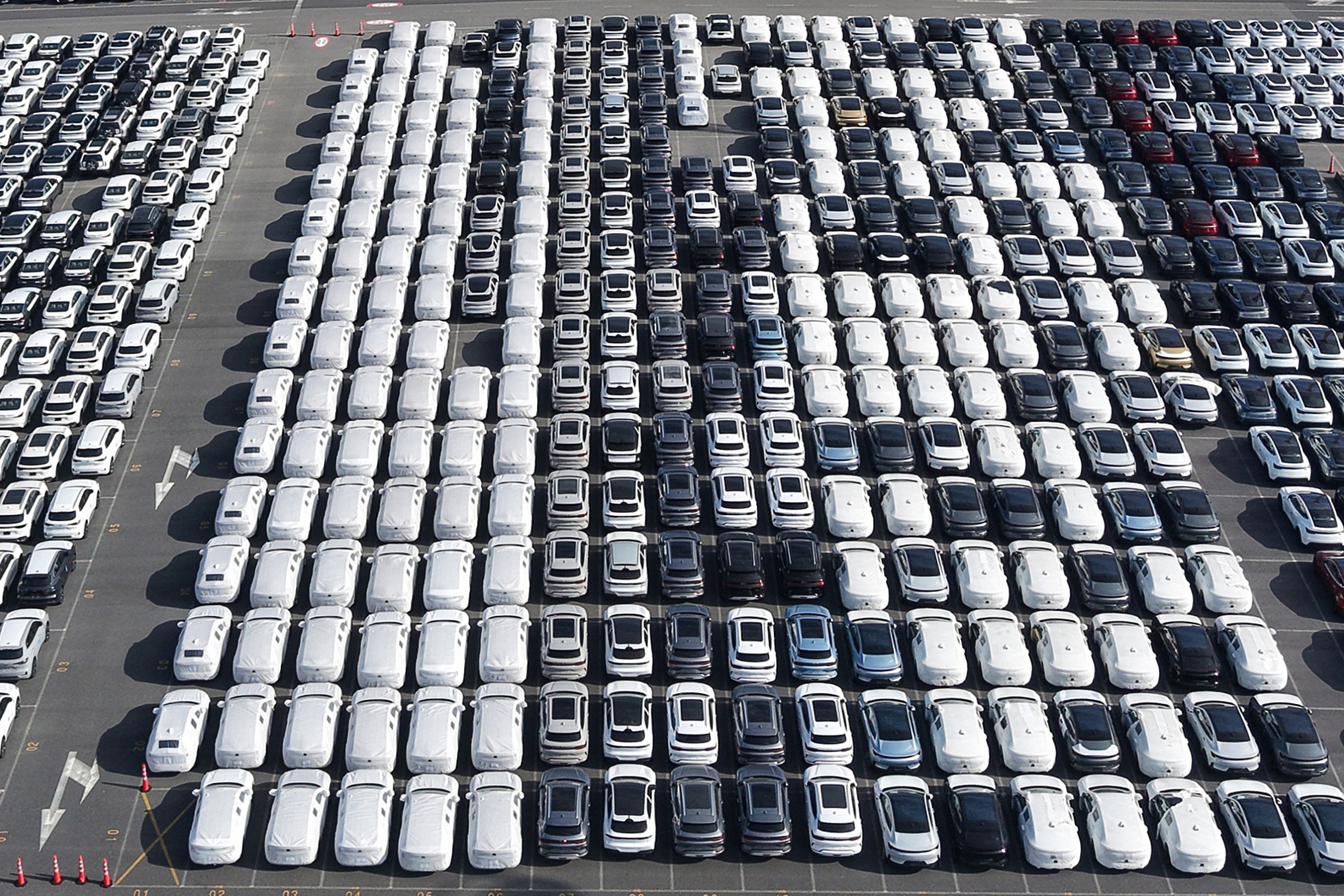 Aerial view of organized parking lot with hundreds of white, black, and gray vehicles arranged in rows