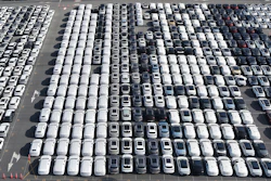 Aerial view of organized parking lot with hundreds of white, black, and gray vehicles arranged in rows