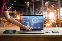 Engineer monitoring industrial control software on laptop in manufacturing facility with robotic equipment