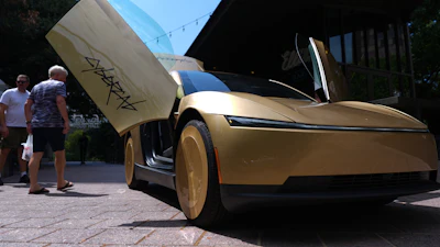 Gold concept car with open gull-wing door displayed at outdoor event with visitors