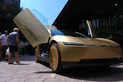 Gold concept car with open gull-wing door displayed at outdoor event with visitors