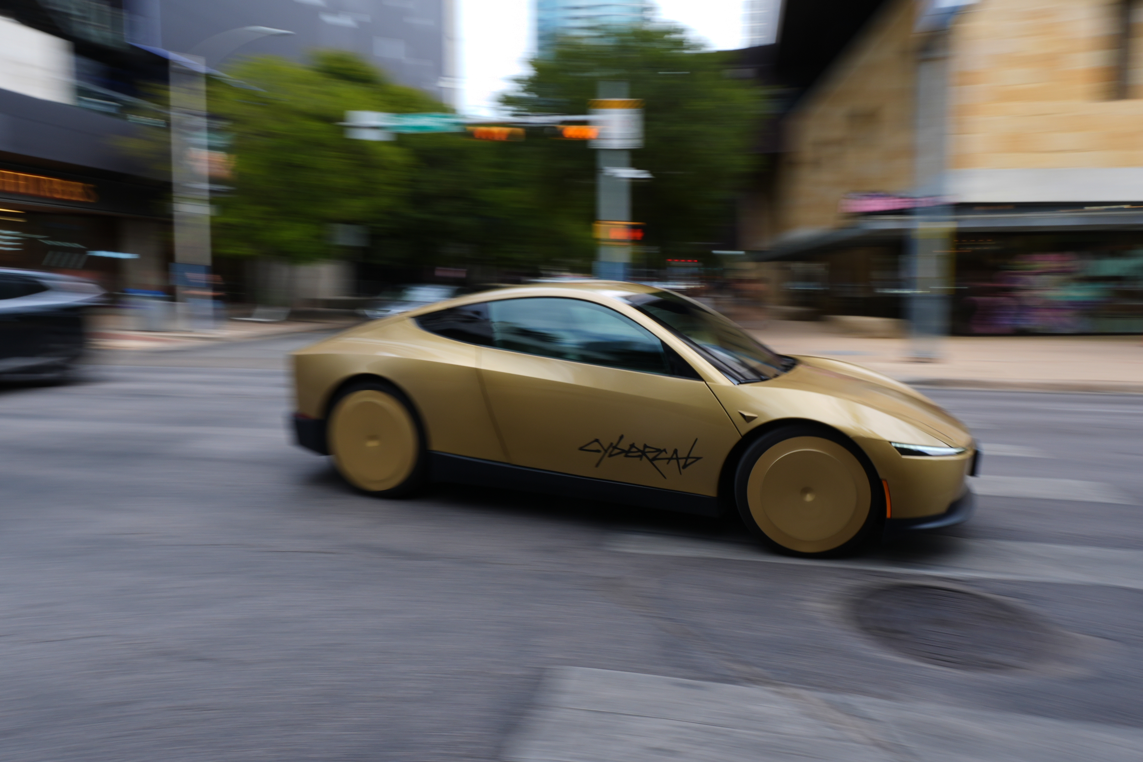 Gold concept sports car with 'Cybertruck' branding driving through urban street with buildings and trees