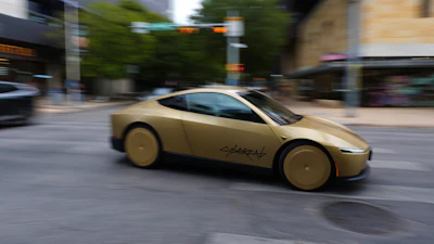 Gold concept sports car with 'Cybertruck' branding driving through urban street with buildings and trees