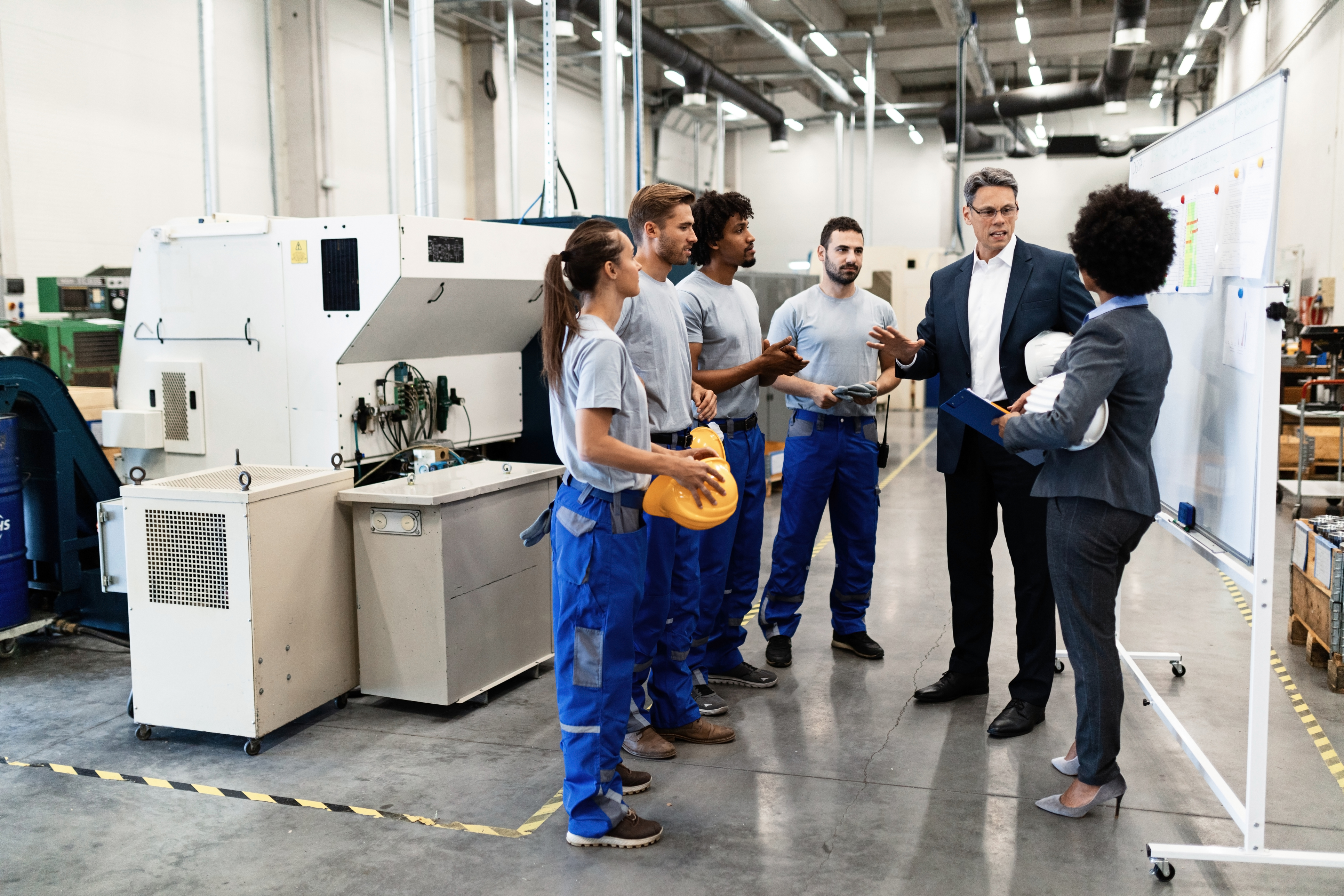 Manufacturing facility tour with workers and business professionals discussing near industrial machinery
