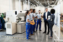 Manufacturing facility tour with workers and business professionals discussing near industrial machinery
