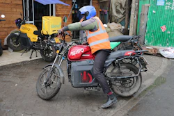 Delivery rider in orange safety vest and blue helmet on Spiro electric motorcycle with delivery box in urban setting