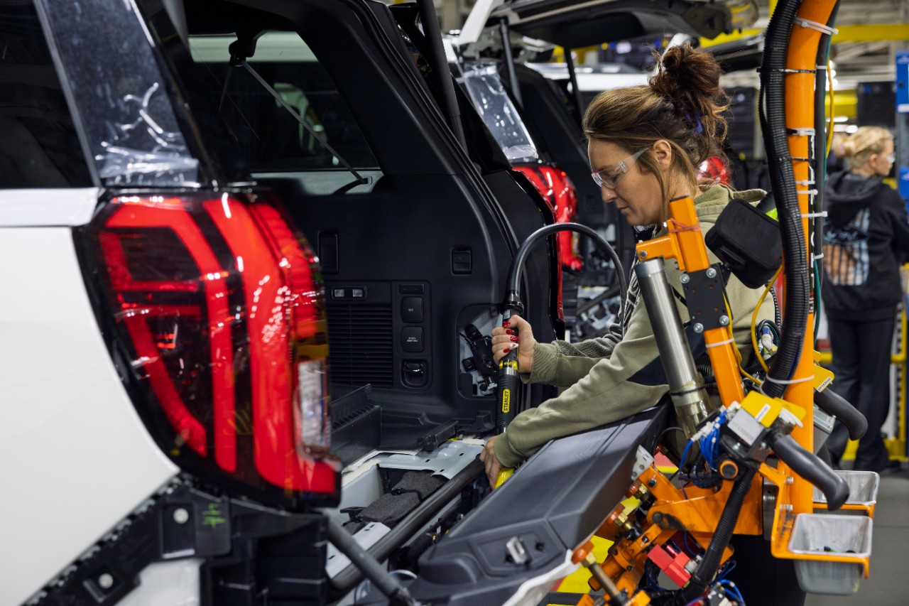 Woman assembling vehicle component in manufacturing facility with red taillight visible