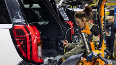 Woman assembling vehicle component in manufacturing facility with red taillight visible