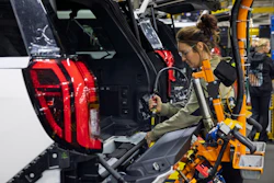 Woman assembling vehicle component in manufacturing facility with red taillight visible