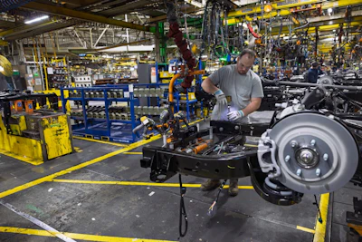 Factory worker assembling automotive axle and brake components on yellow-marked production line in manufacturing facility