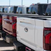 Row of white and red Ford pickup trucks parked in outdoor dealership lot with clear sky