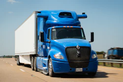 Blue Peterbilt semi-truck with white refrigerated cargo trailer driving on highway