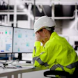 Construction worker in safety gear analyzing data charts on computer monitor in industrial facility