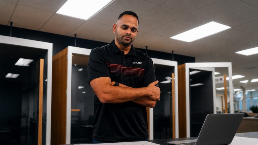 Professional man in black GMC polo shirt standing confidently in modern server room with laptop
