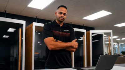 Professional man in black GMC polo shirt standing confidently in modern server room with laptop