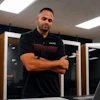 Professional man in black GMC polo shirt standing confidently in modern server room with laptop