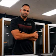 Professional man in black GMC polo shirt standing confidently in modern server room with laptop