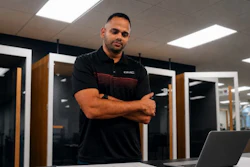Professional man in black GMC polo shirt standing confidently in modern server room with laptop