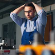 Technician in blue overalls and glasses adjusting his hair in an industrial workshop with equipment on the workbench