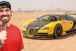 Content creator in red shirt holding microphone next to yellow and black Bugatti Veyron in desert with city skyline