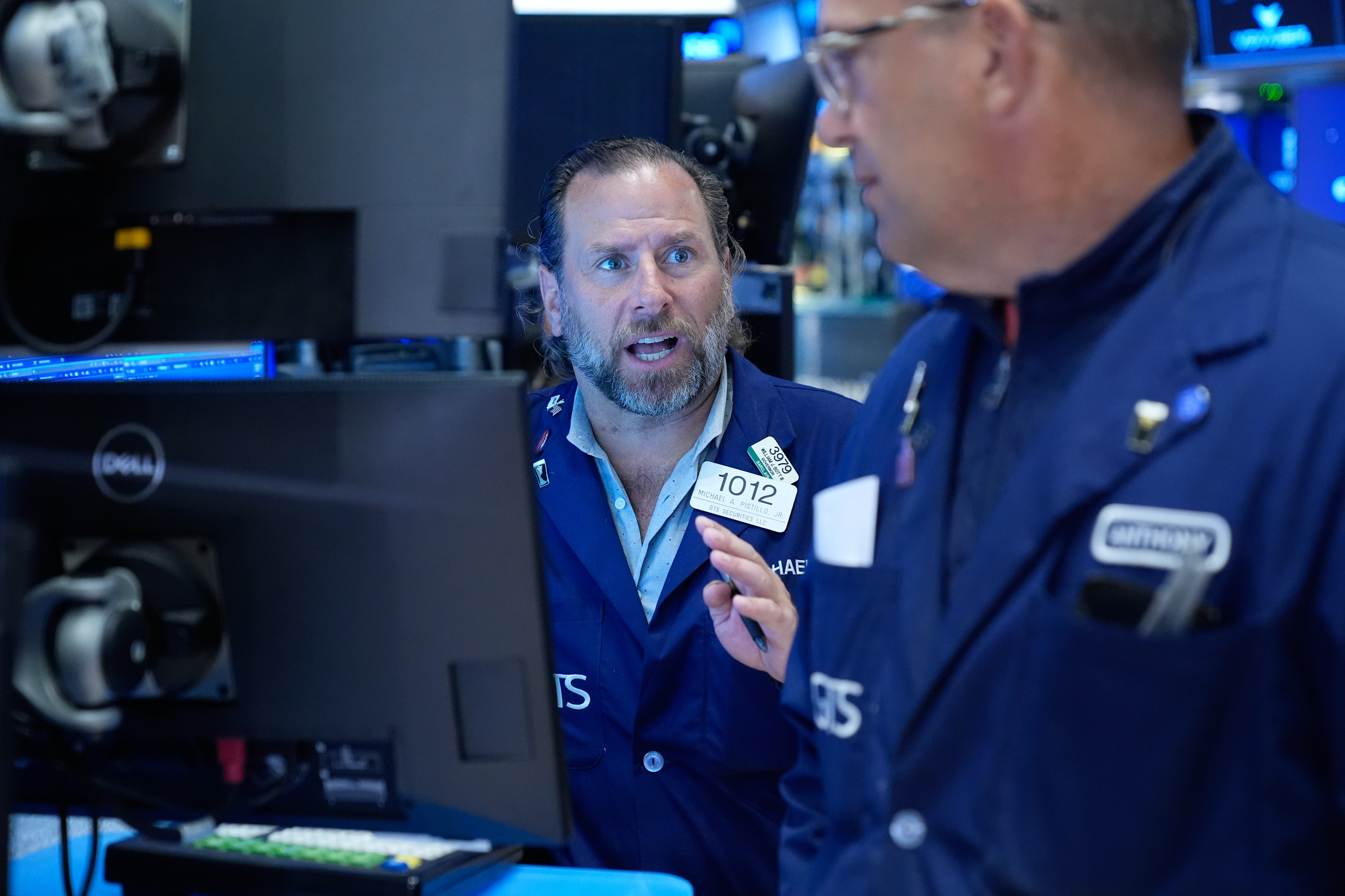 Stock exchange traders in blue jackets discussing market activity on trading floor with computer monitors