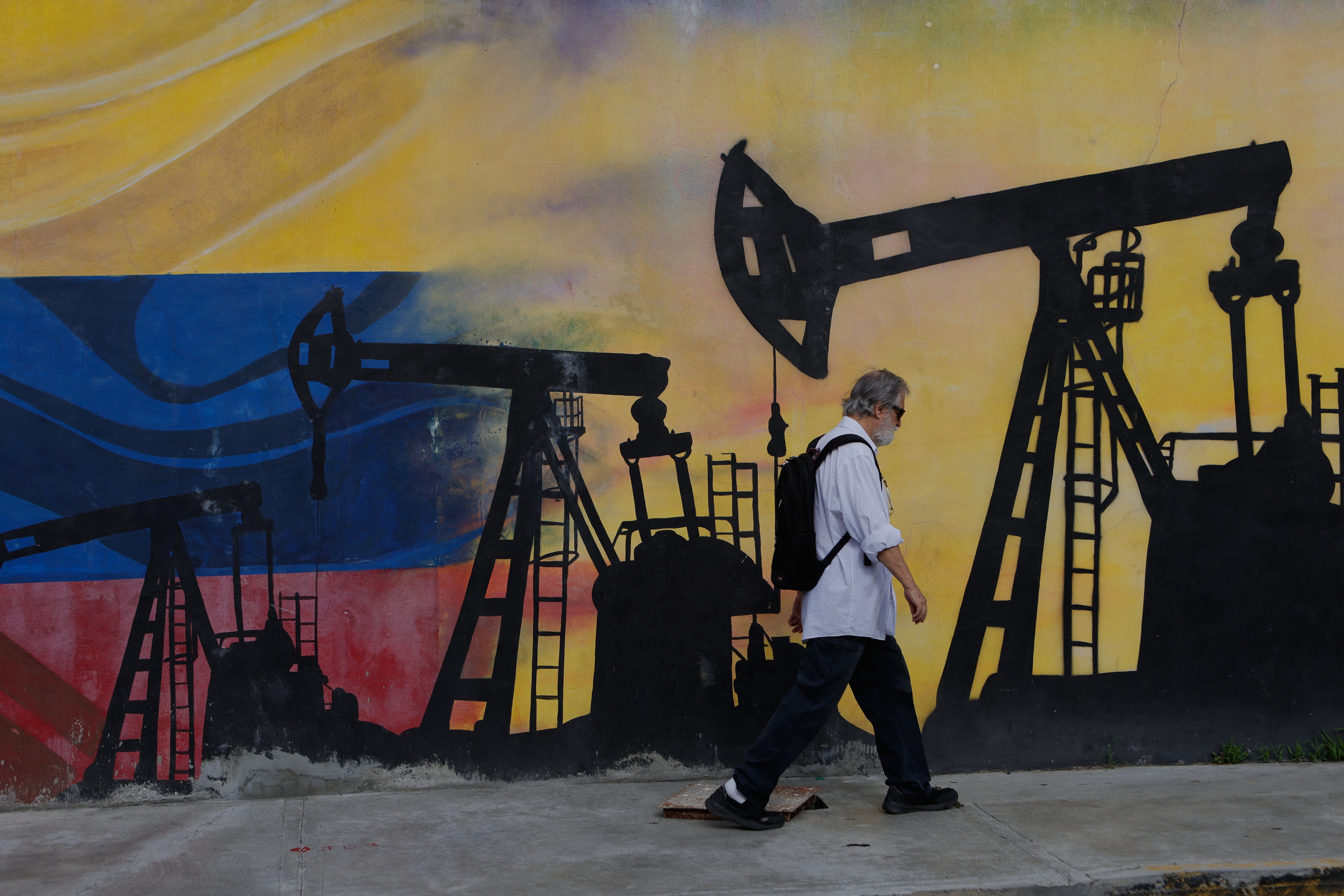 Street mural featuring oil pump silhouettes against Russian flag colors with pedestrian walking past