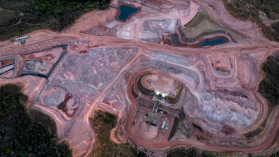 Aerial view of active mining quarry with excavation equipment, earthen pits, and surrounding forest