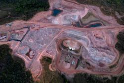 Aerial view of active mining quarry with excavation equipment, earthen pits, and surrounding forest