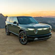 Rivian R1S electric SUV parked on a mountain overlook at sunset with rolling hills in background