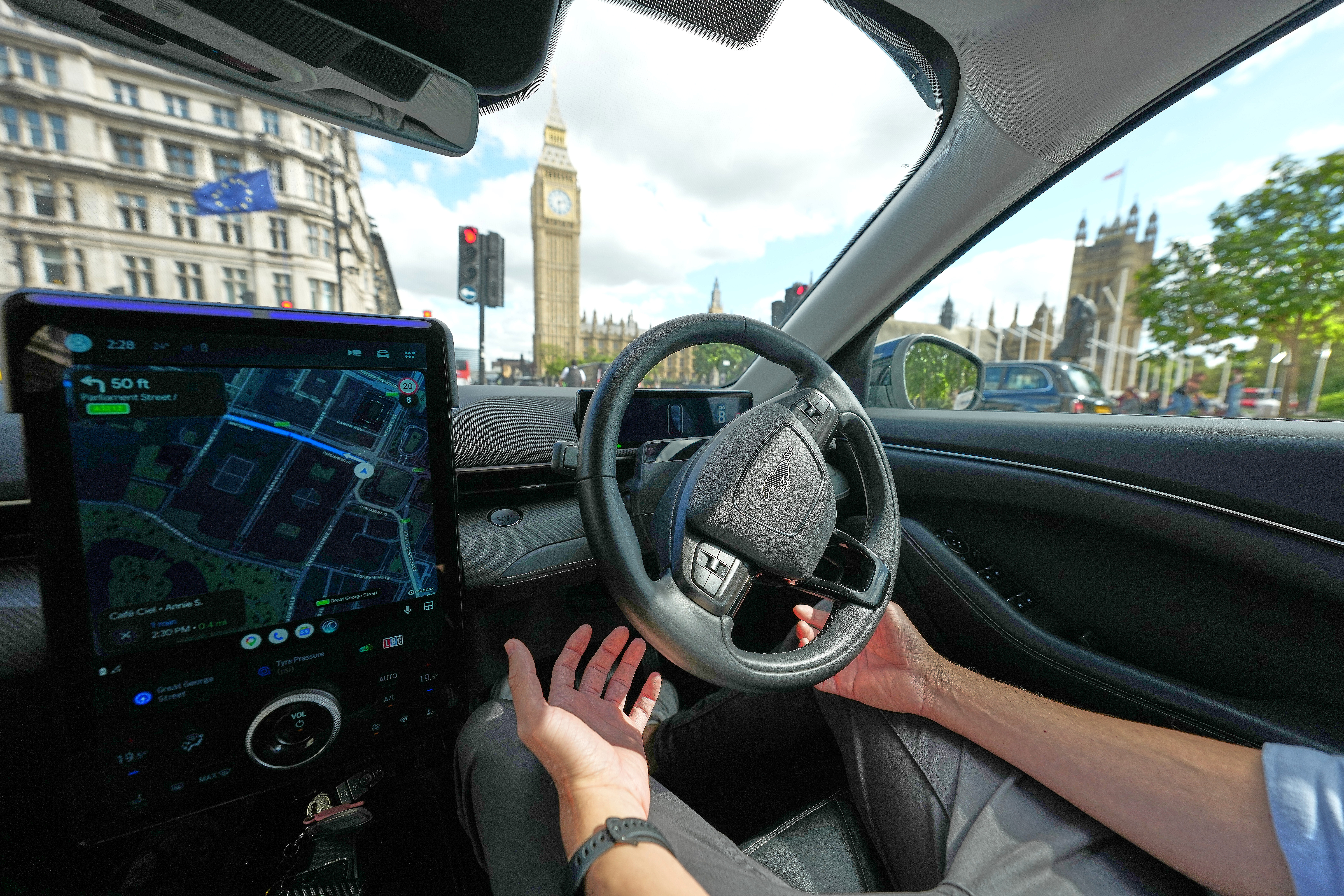 Driver's view from inside a car with GPS navigation display, steering wheel, and London's Big Ben visible through windshield