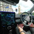 Driver's view from inside a car with GPS navigation display, steering wheel, and London's Big Ben visible through windshield