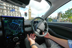 Driver's view from inside a car with GPS navigation display, steering wheel, and London's Big Ben visible through windshield