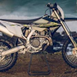 White and black dirt bike motorcycle on stand against cloudy sky and desert landscape