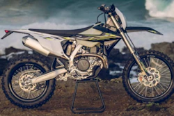 White and black dirt bike motorcycle on stand against cloudy sky and desert landscape