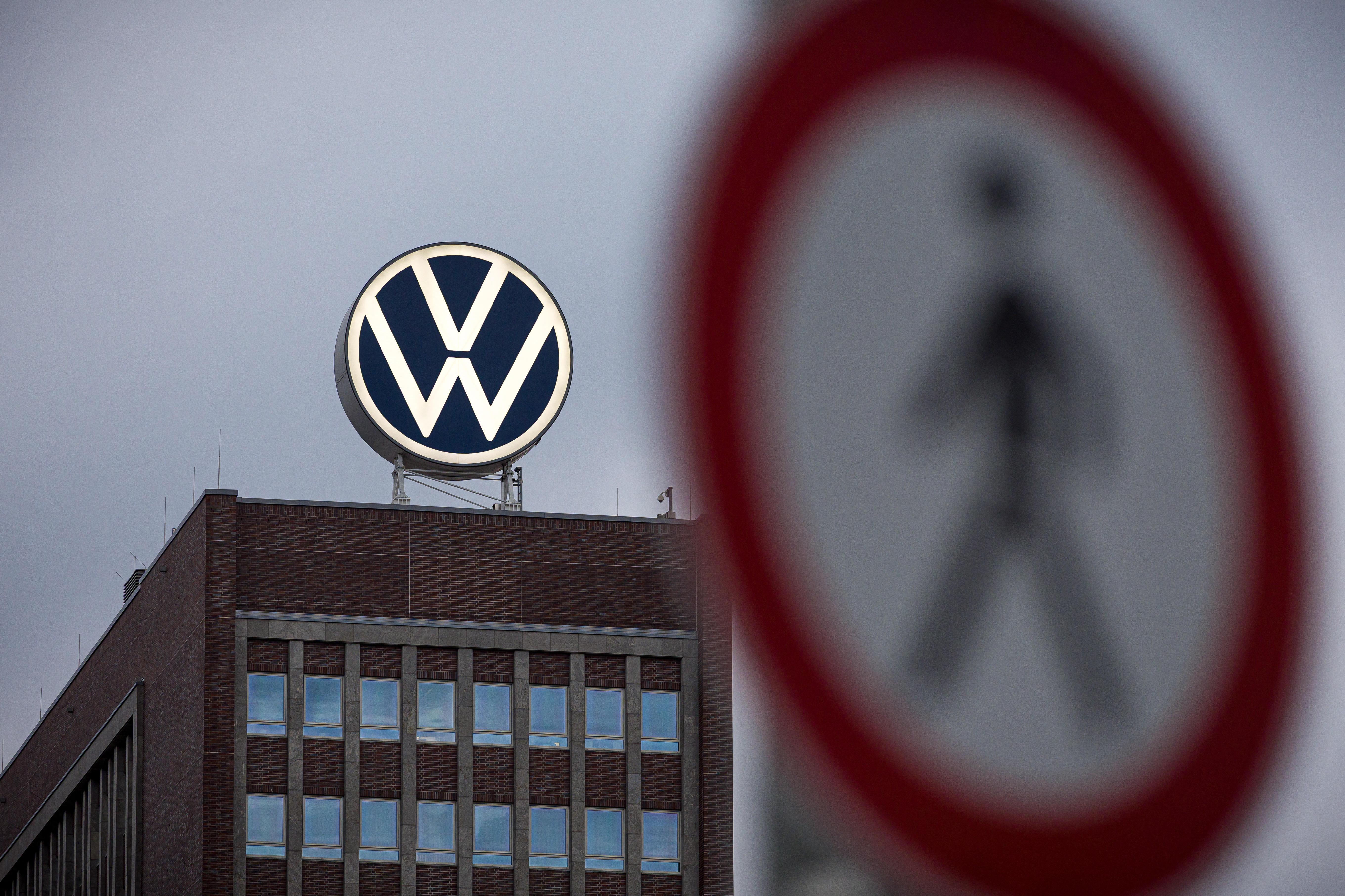 Volkswagen logo mounted on rooftop of brick building with pedestrian crossing sign in foreground