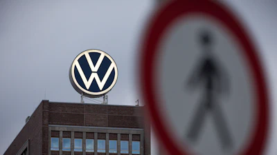 Volkswagen logo mounted on rooftop of brick building with pedestrian crossing sign in foreground
