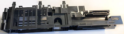Disassembled black plastic electronic device component with ventilation slots and mounting hardware