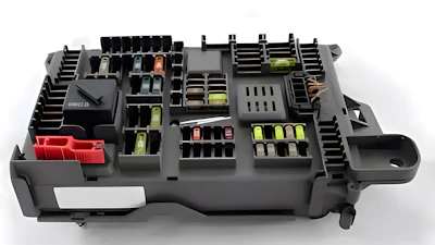 Automotive fuse box with organized yellow and red fuses, relays, and electrical components in black housing