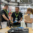 Trade show booth demonstration with staff and visitors examining tools and equipment at an industrial exhibition