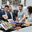 Professionals examining tools and equipment at a trade show booth with green lanyards