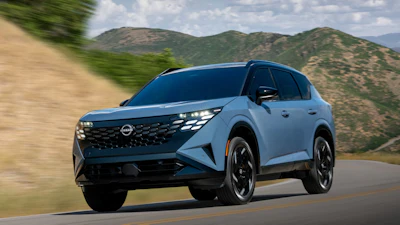 Light blue Nissan Ariya electric SUV driving on a mountain road with scenic hills in the background