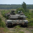 Military tank positioned in forested terrain with coniferous trees and cleared ground in background