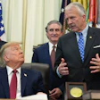 Formal meeting in the Oval Office with government officials and American flags in background