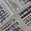 Aerial view of a large parking lot with hundreds of white, gray, and black vehicles arranged in organized rows