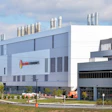 Modern industrial facility with Helios Technologies signage, featuring blue and white architecture with cylindrical ventilation stacks on the roofline.