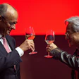 Two professionals toasting with glasses of whiskey against a red background during a formal event