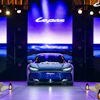 Luxury sports car displayed on stage during brand launch event with illuminated screens and dramatic blue lighting