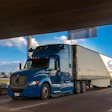 Blue Schneider semi-truck with white refrigerated trailer driving on highway under overpass