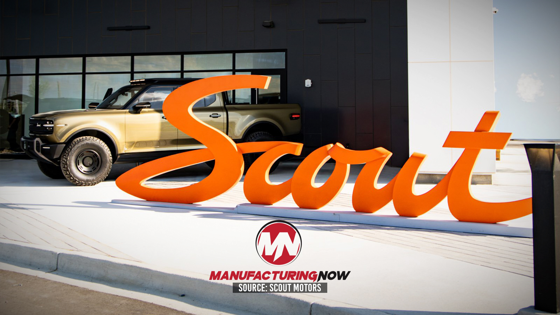 Scout Motors orange brand signage displayed outside showroom with tan SUV and Manufacturing Now logo